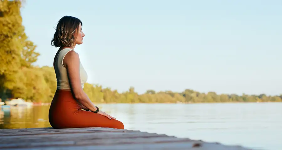 mujer sentada frente un lago en actitud pacífica