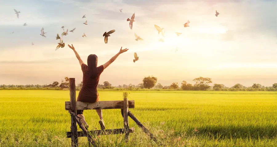 mujer en un campo con los brazos en alto junto a palomas volando