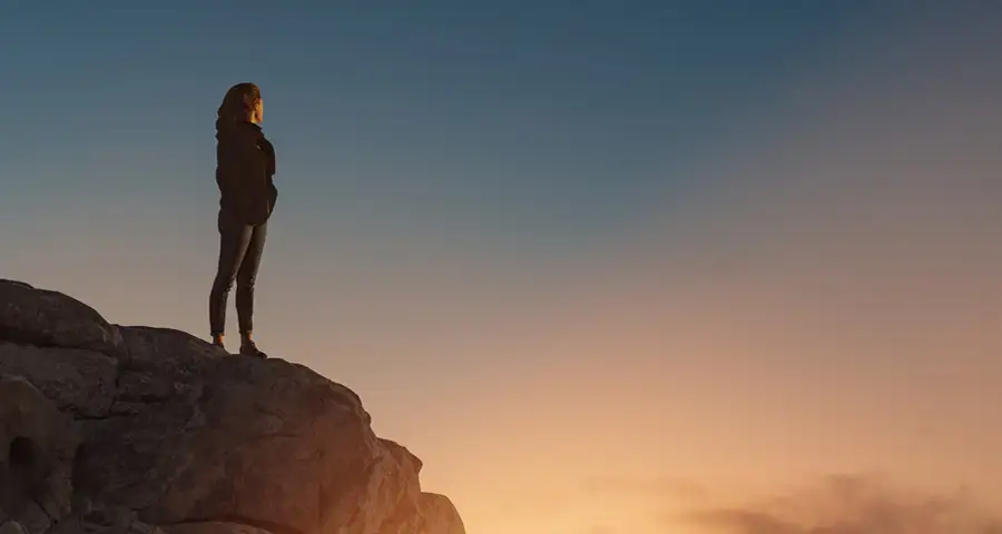 mujer en lo alto de una montaña al atardecer