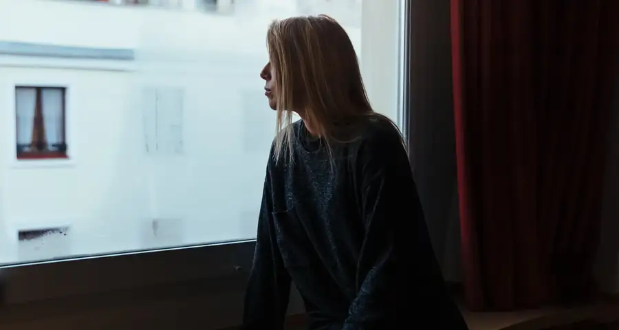 mujer con mirada melancólica mirando por la ventana